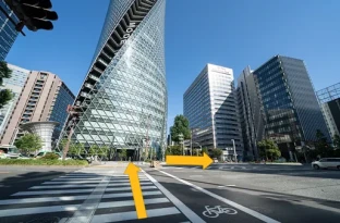 画像：ルート説明4　螺旋状のビルの「名古屋モード学園スパイラルタワー」側に横断歩道を渡って、右折してまた横断歩道を渡ります。